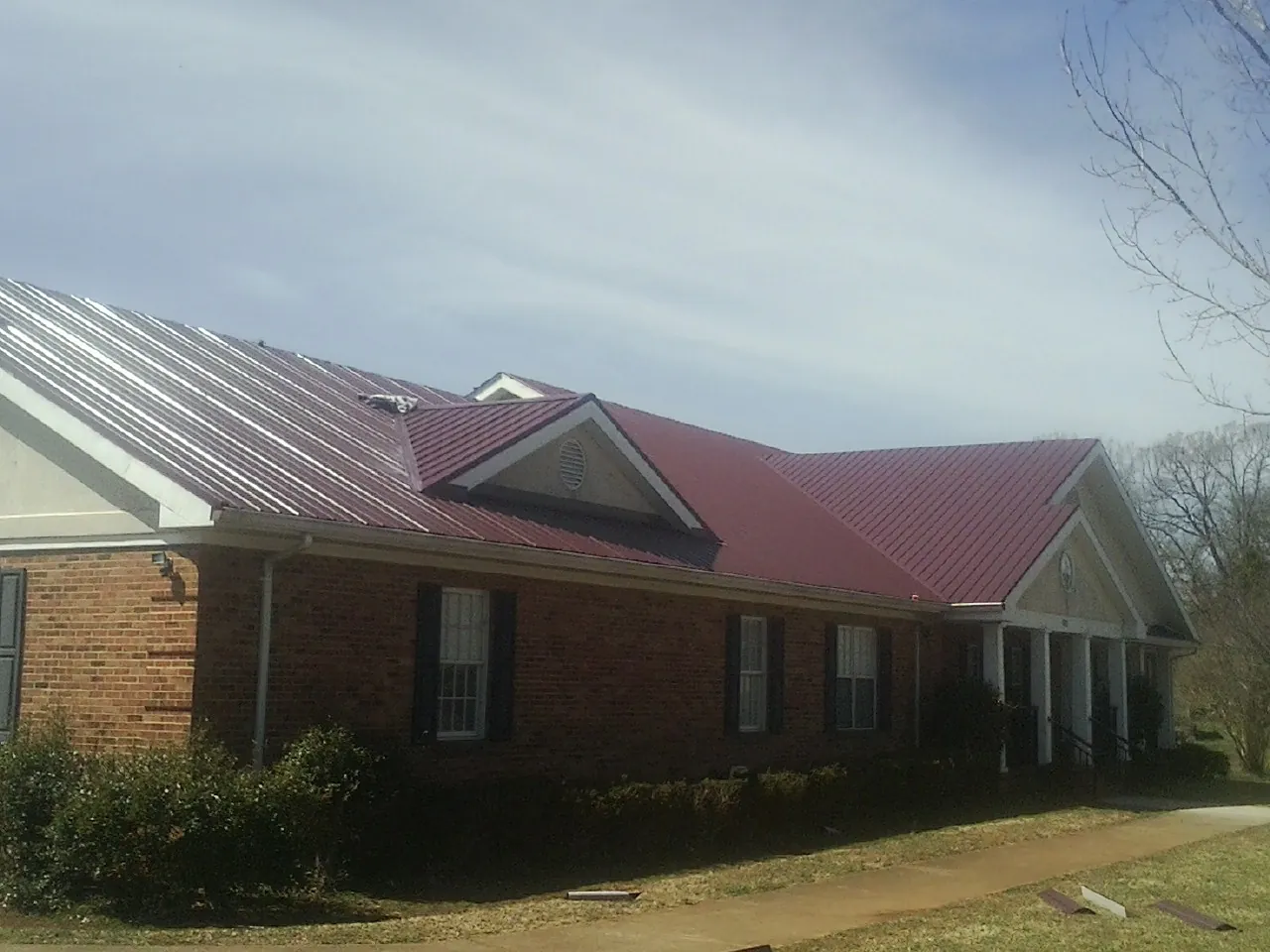 Red metal roof with gabled entries on a long brick building, from a Hail Damage Roof Repair job in Manilla