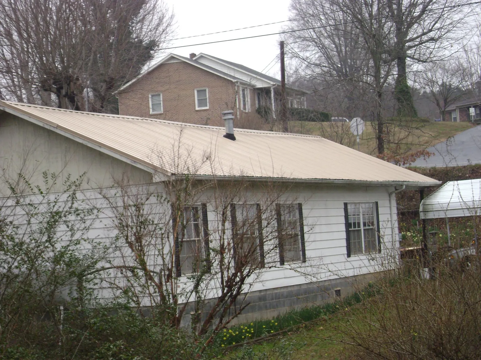 Tan metal roof on a white sided house set into a hillside — Commercial Roofing by Roofing Brothers in Manilla